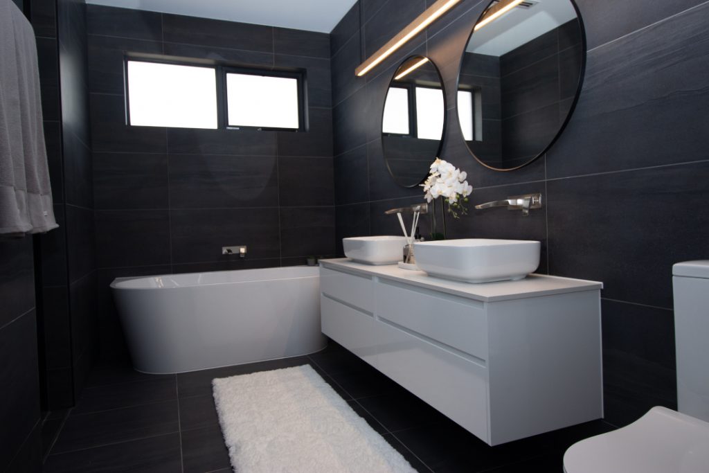 Black tiled bathroom with a bath tube and two sinks