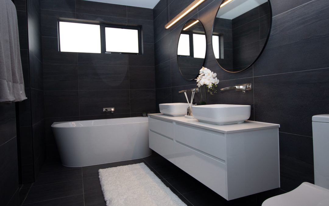 Black tiled bathroom with a bath tube and two sinks